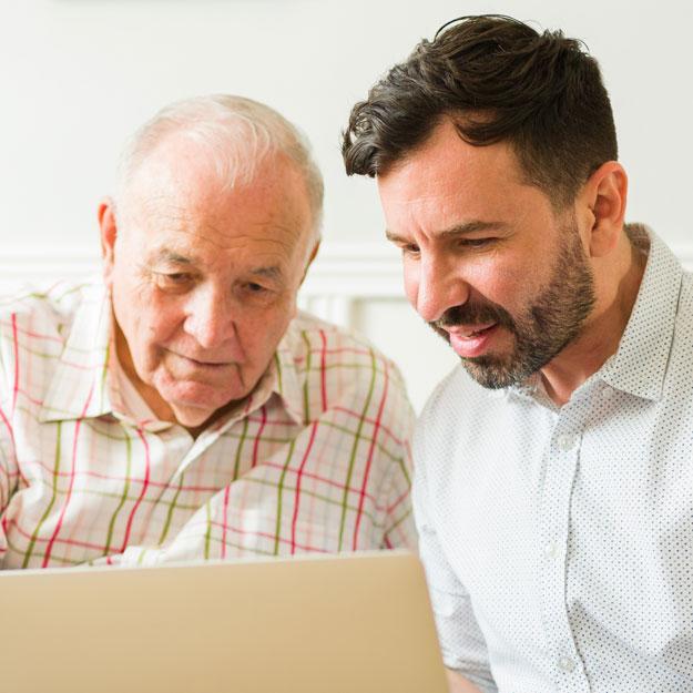 Older man helping younger man use a laptop